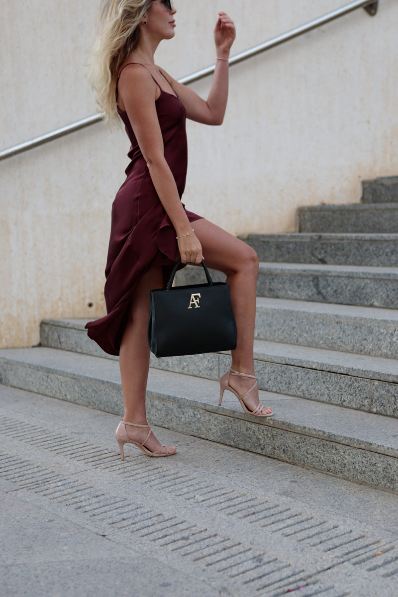 Navona, top-handle bag in black honeycomb-embossed Italian leather – carried by hand on stone steps