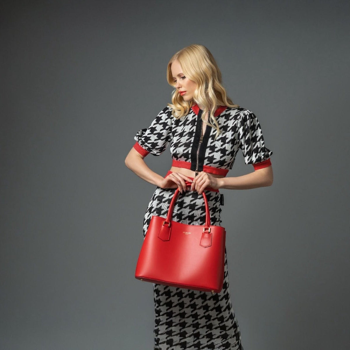 Woman in a houndstooth dress holding a red Italian leather tote, a key colour for autumn-winter 2026