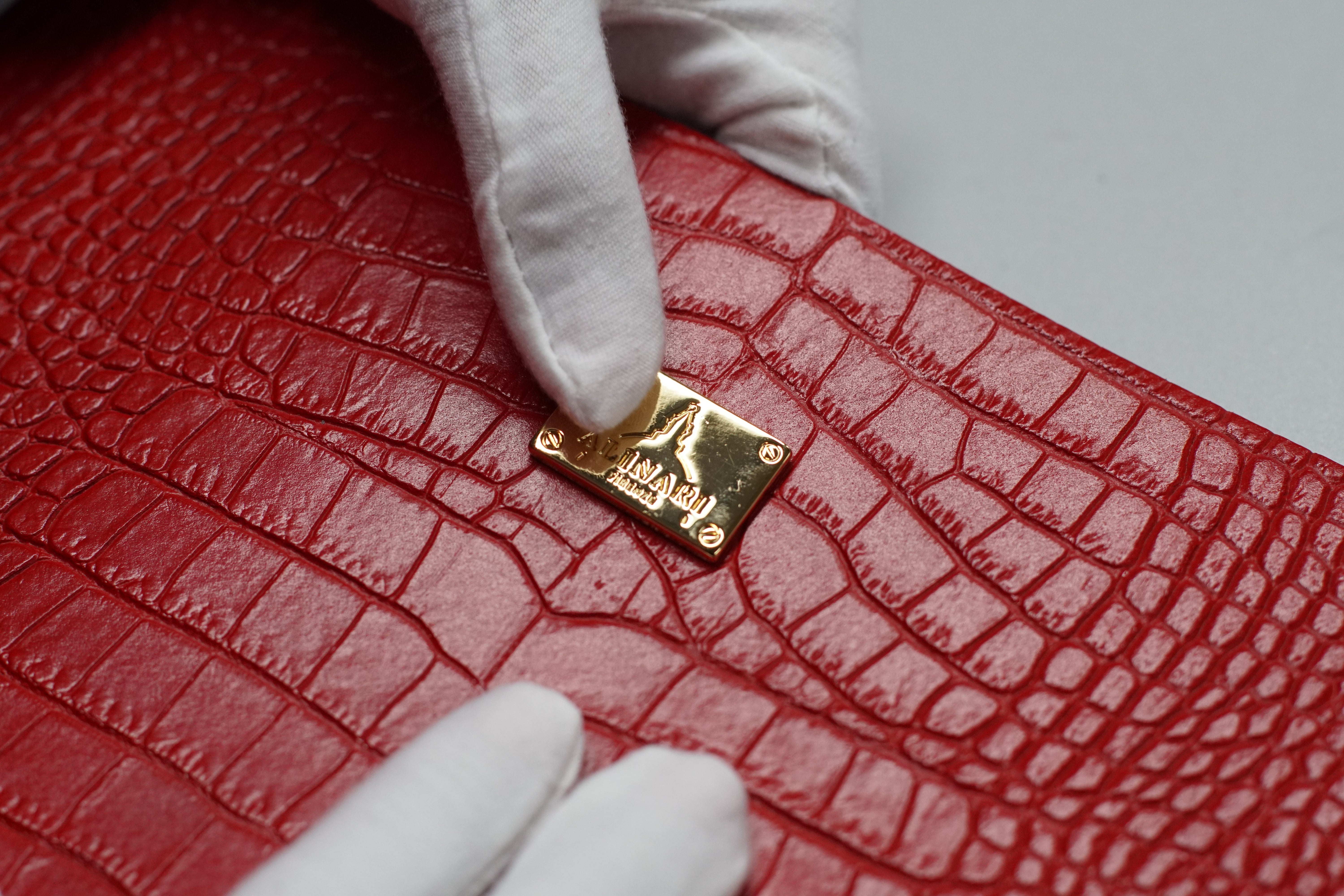 Gloved hands showing red croc-embossed leather with the gold AF logo