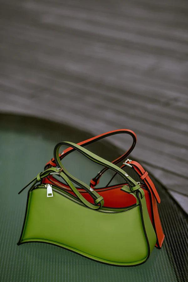 An Ala Shoulder Bag by Alinarifirenze, a fashionable handbag in green and orange, made with premium materials, sitting on a table.
