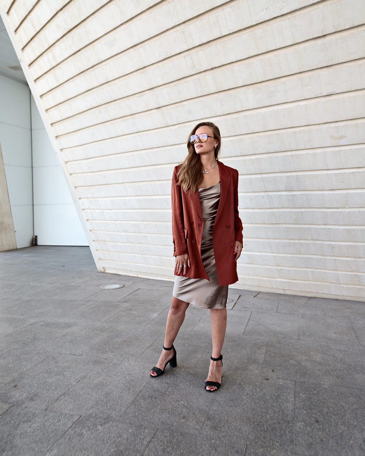 Autumn outfit with a rust linen blazer, champagne satin dress and Toscana sunglasses against pale stone architecture in Valencia