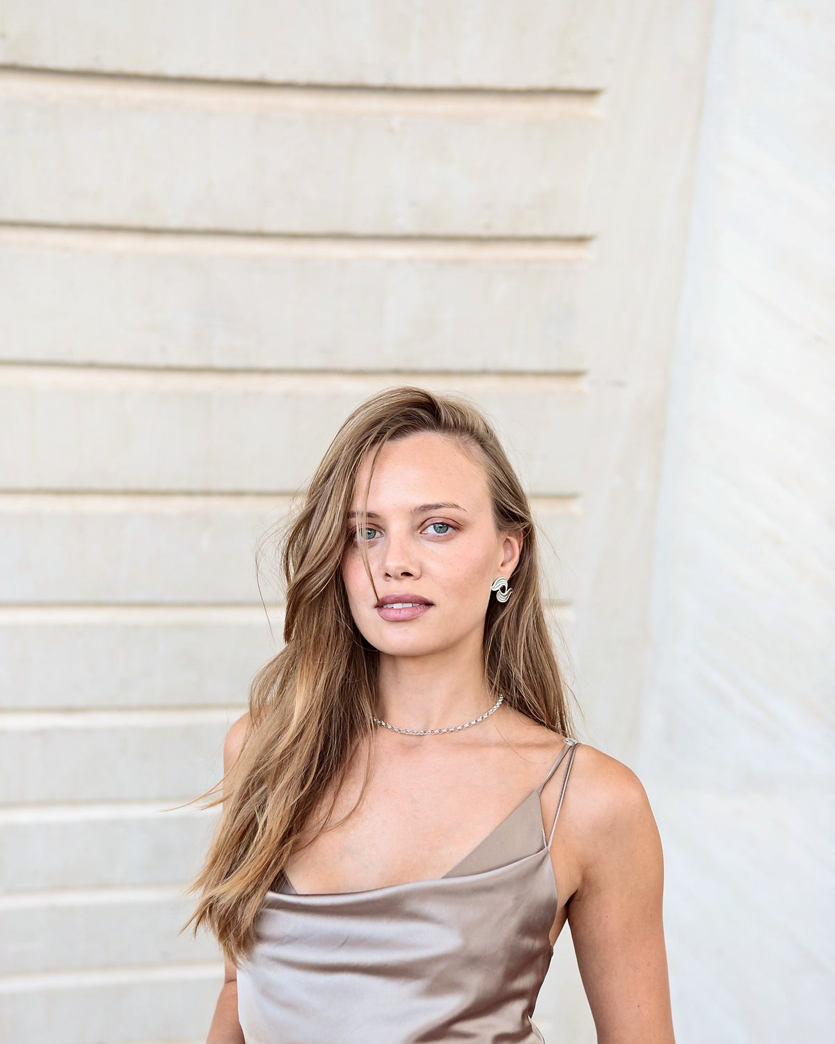 Portrait in a champagne satin slip dress against a pale stone wall in Valencia, from the Alinari autumn lookbook