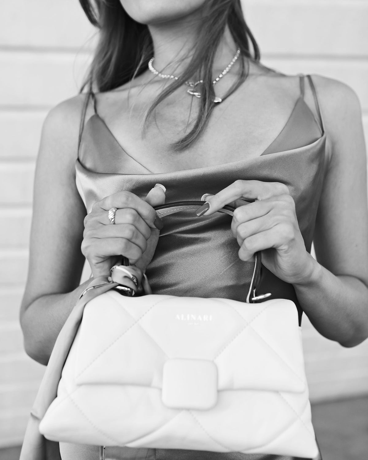 Black and white close-up of the Alita quilted leather handbag held with a satin slip dress